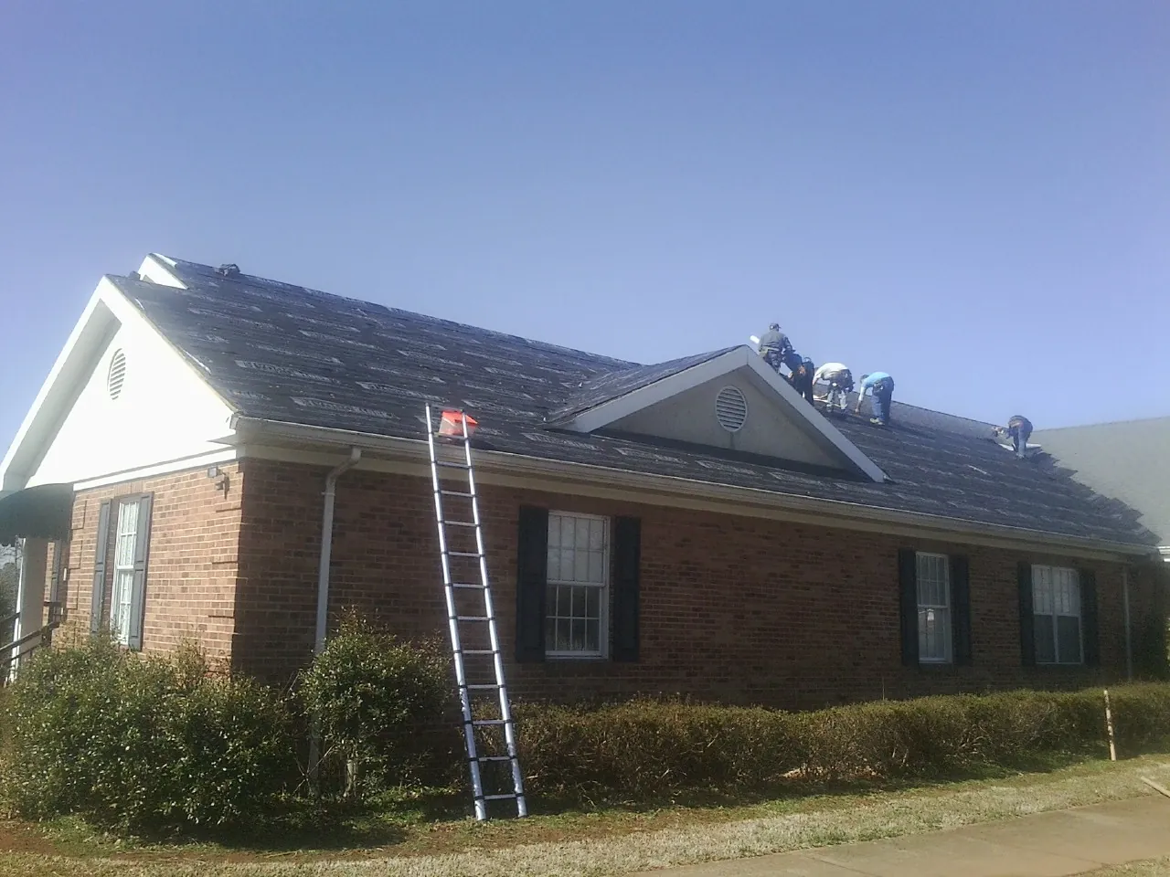 Crew tearing shingles off a brick ranch roof with a ladder set — Metal Roof Repair work by our crew in Paoli