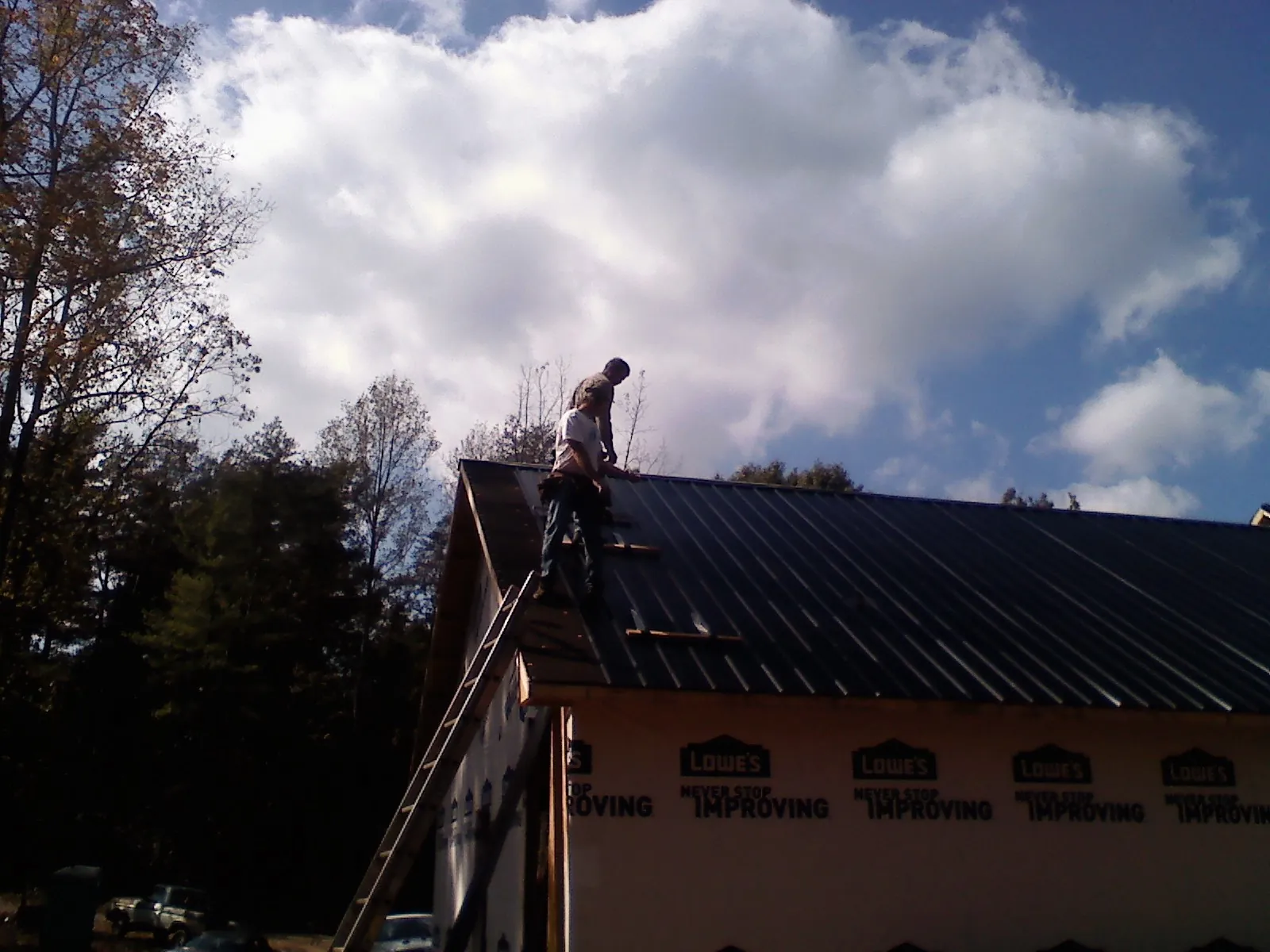 Roofer fastening dark metal panels high against a cloudy sky, from a Roof Inspection job in Paoli