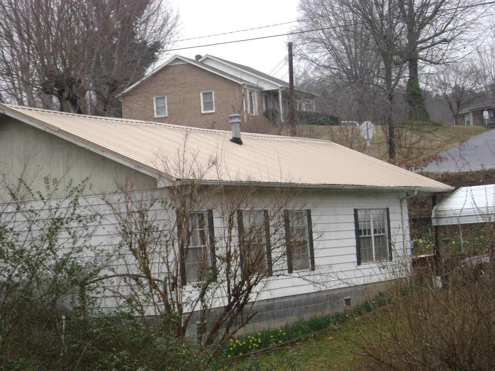 Tan metal roof on a white sided house set into a hillside — Commercial Roofing by Roofing Brothers in Paoli